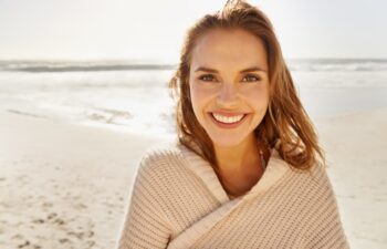 Travel, portrait and happy woman at a beach for summer, break or vacation, adventure or holiday. Ocean, face and female person smile at the sea with freedom, good mood or solo trip in South Africa